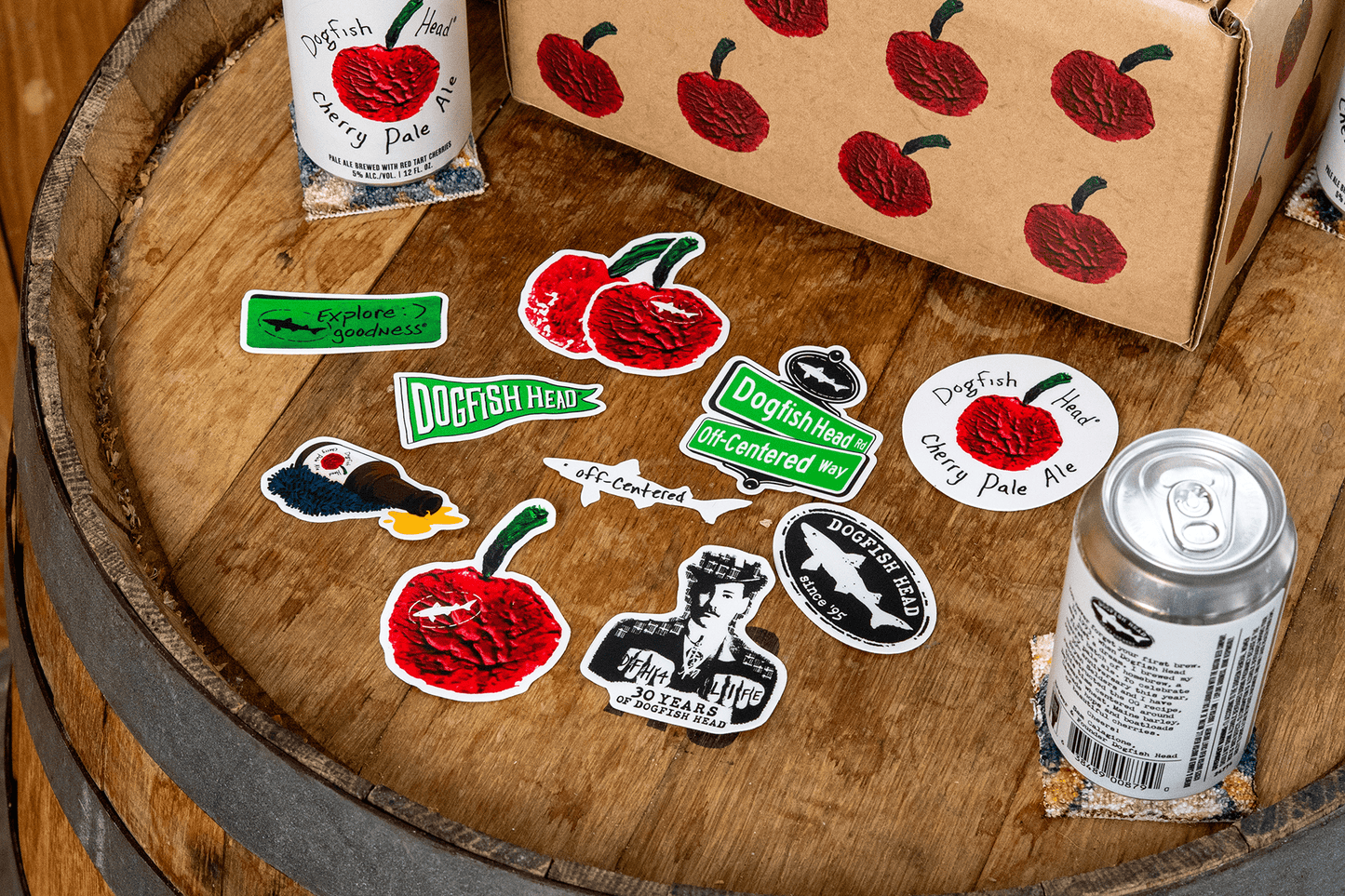 Dogfish Head Stickers and a can on a wooden barrel with a box.