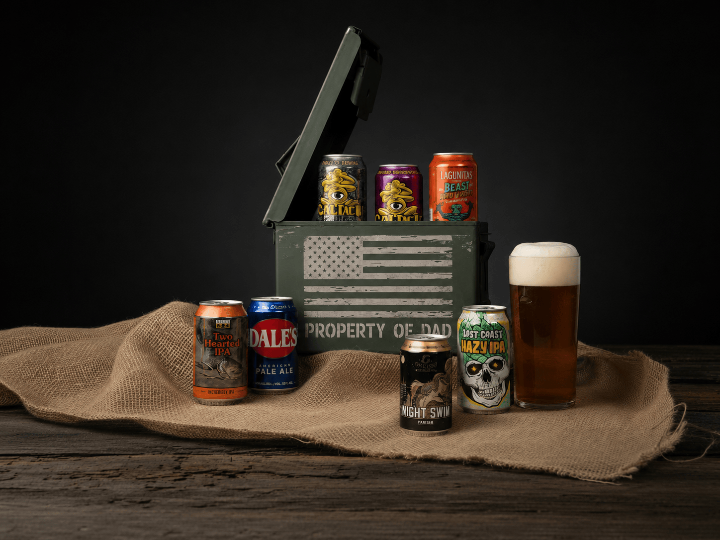 Collection of beer cans and a glass of beer on a wooden surface with a black background.