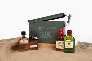 Four top-shelf whiskey bottles displayed inside open ammo can – premium whiskey gift idea