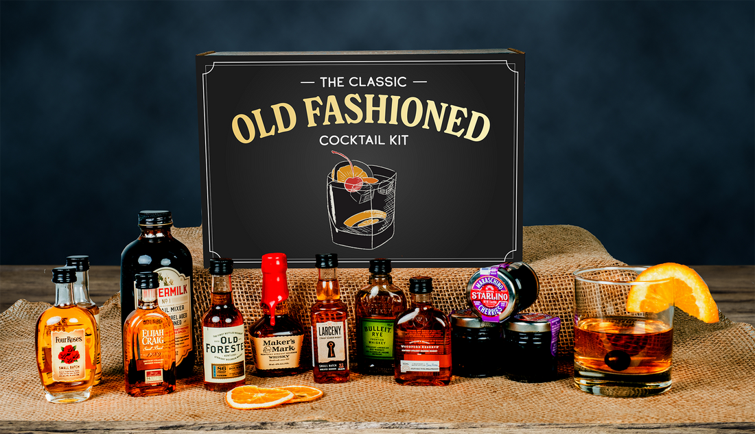 Classic Old Fashioned Kit from GiveThemBeer with eight whiskey bottles, mixer, and garnishes on a wooden table
