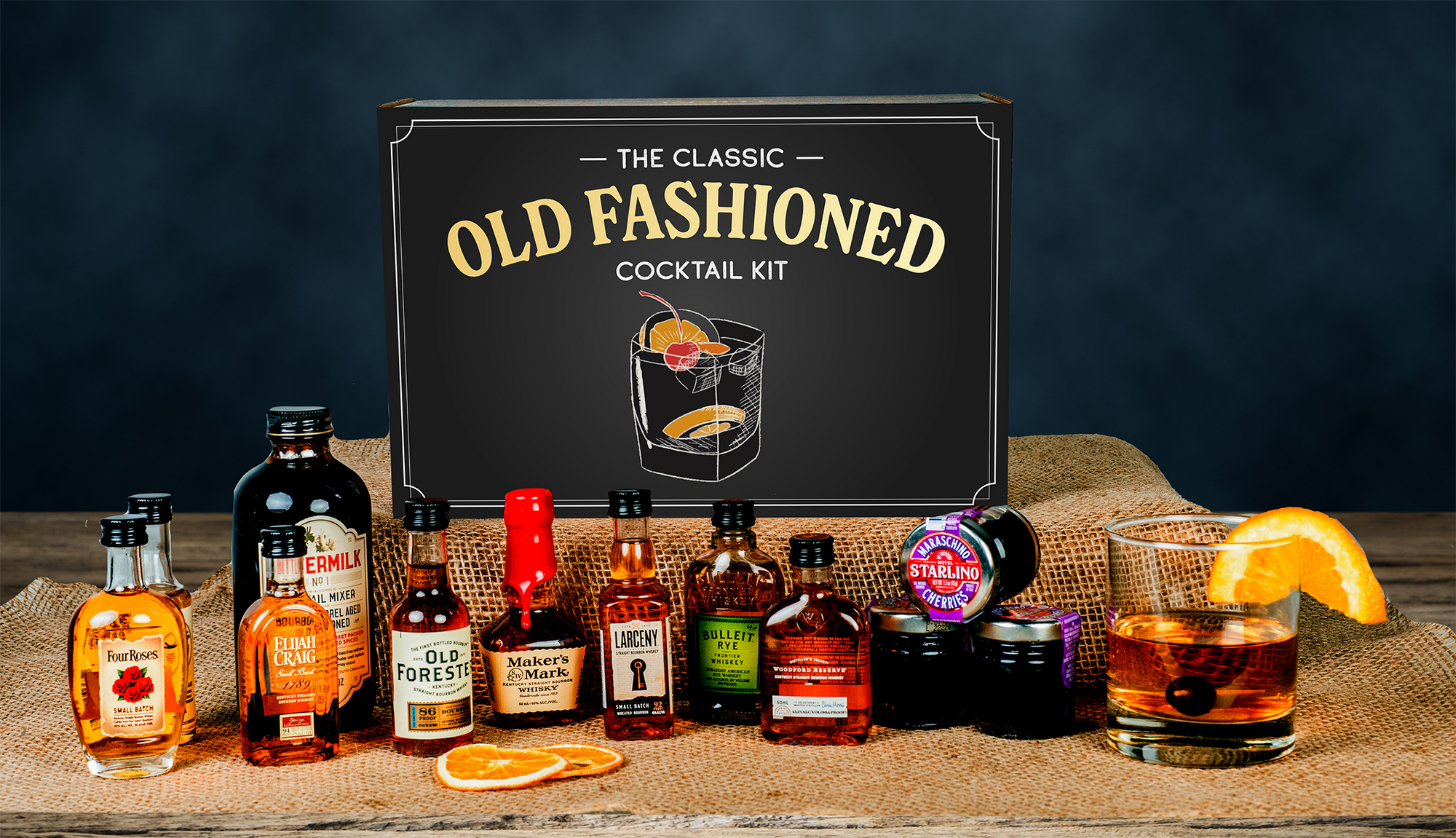 Classic Old Fashioned Kit from GiveThemBeer with eight whiskey bottles, mixer, and garnishes on a wooden table