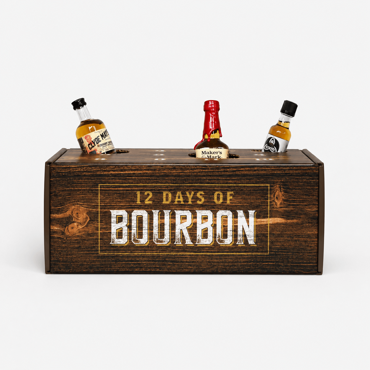 A dark brown wooden gift box engraved with '12 DAYS OF BOURBON' in white and gold lettering, holding three miniature liquor bottles on a light gray background.