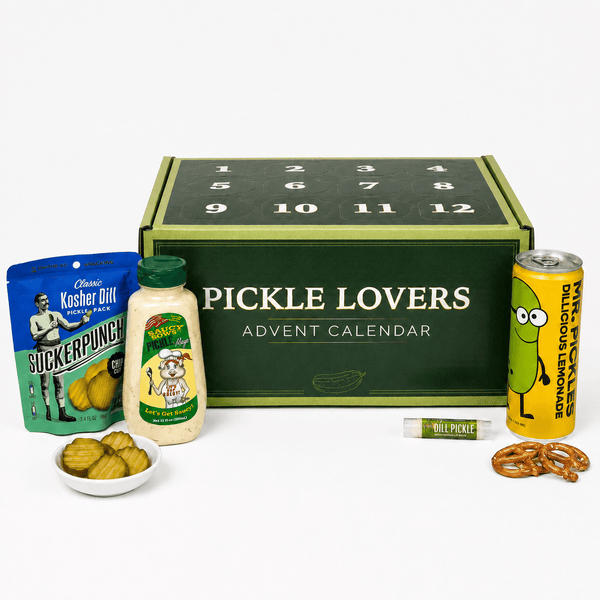 Pickle Lovers Advent Calendar gift set on a white background, featuring a dark green numbered box with mustard-green trim, surrounded by themed snacks including a bag of Kosher Dill pickles, a jar of relish, a can of lemonade, pretzels, and a small bowl of pickled onions.