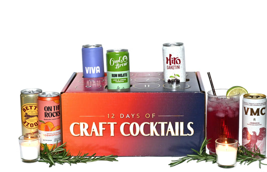 A craft cocktail subscription box labeled '12 DAYS OF CRAFT COCKTAILS' in orange and navy, surrounded by assorted canned cocktails, a prepared drink with lime and a glass, candles, and rosemary sprigs on a white background.