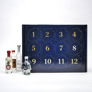 A 12-day liquor advent calendar with a dark navy blue textured cover and gold numbers, shown with several small bottles of spirits arranged in front on a white studio background.