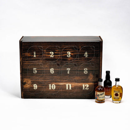 A rustic dark wood 12-day advent calendar box with numbered windows, shown next to three mini bourbon bottles on a clean white background.