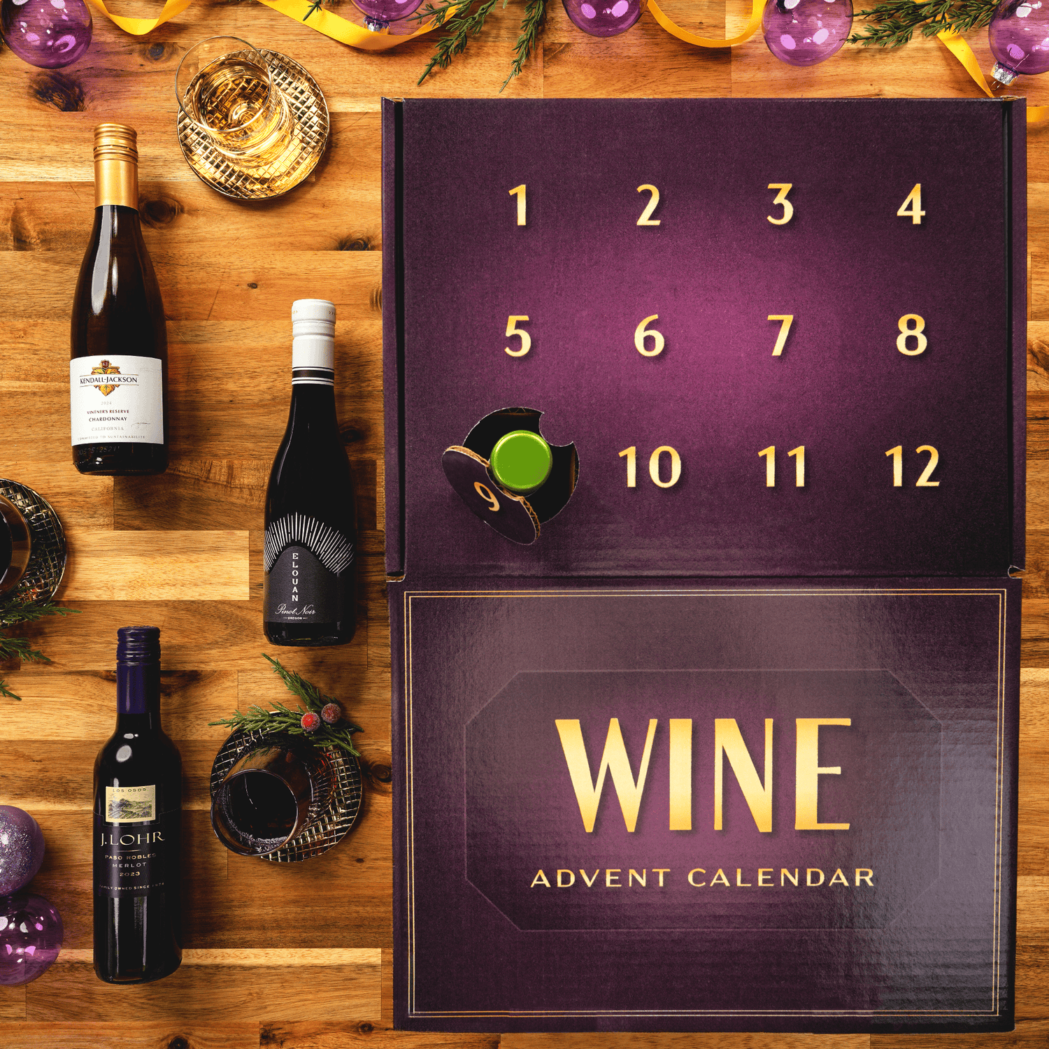 A wine-themed 12 day advent calendar box on a wooden table, shown alongside several wine bottles and festive decorations. The calendar is dark purple with gold numbers and the words 'WINE ADVENT CALENDAR.